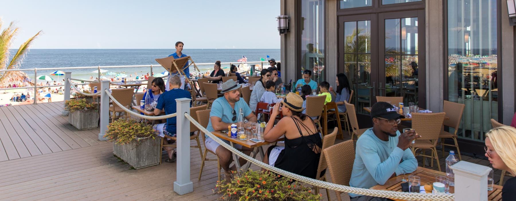 a group of people sitting at tables outside a restaurant near a beach